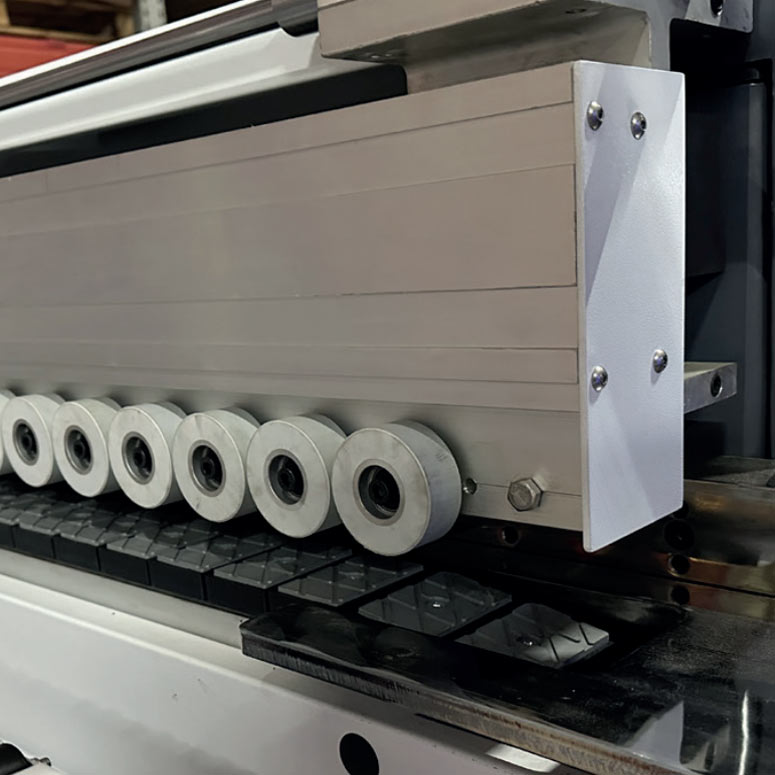 Close-up of a white industrial machine beam fitted with a row of circular pressure rollers above black guide blocks