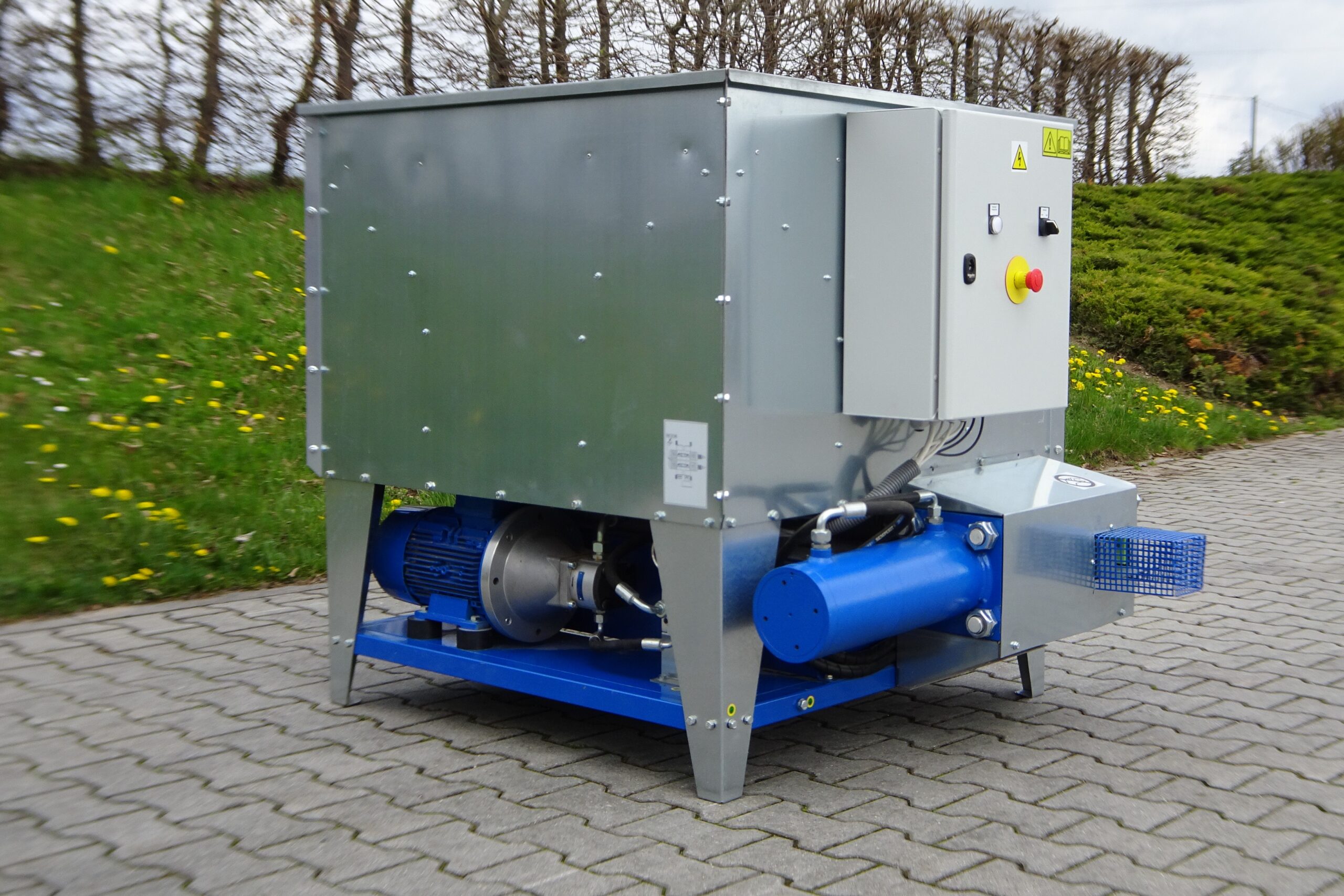 BrikStar EK 20 industrial briquetting machine with blue hydraulic unit and grey steel casing, mounted on a blue steel frame outdoors
