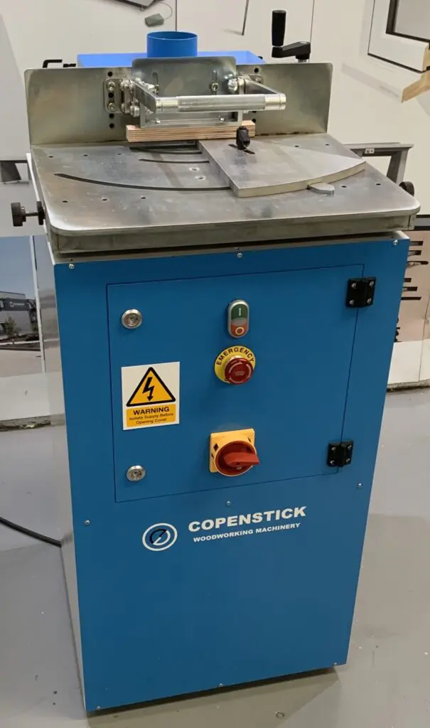 Copenstick end scribe machine with blue cabinet, emergency stop button, isolator switch, and metal worktop for window beading profiles