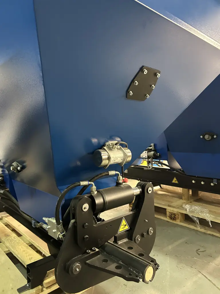 Close-up of a blue Falach 50XL briquette machine showing hydraulic arms, a motor, and mounting bracket on a pallet