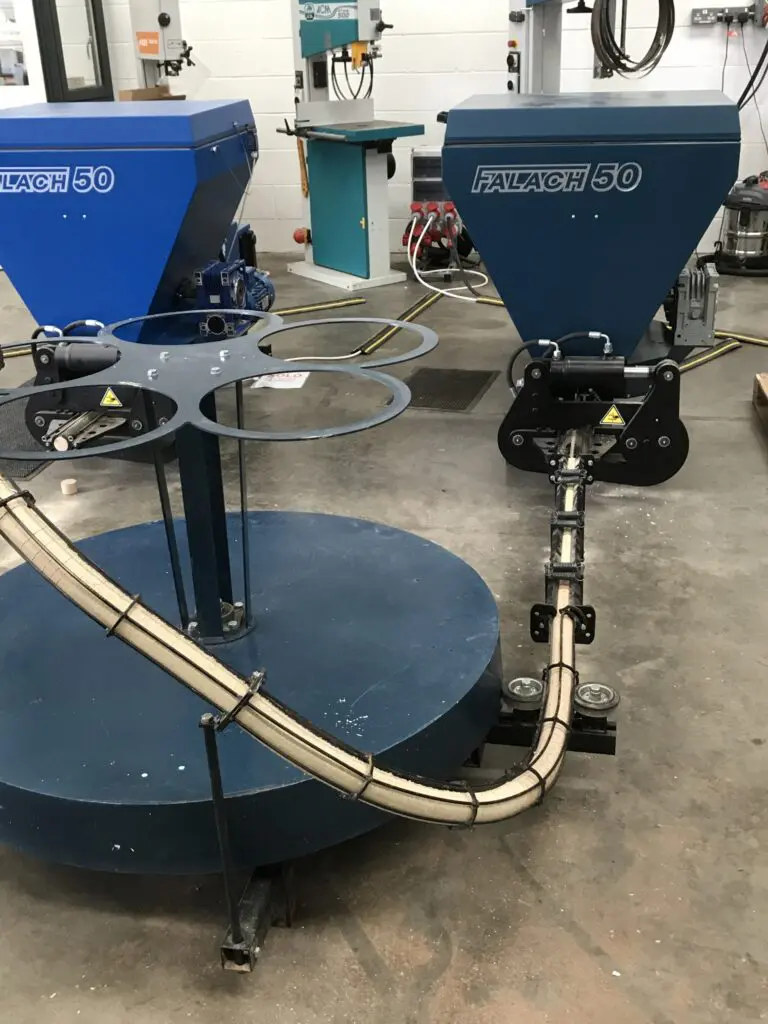 Two blue Falach 50 briquette machines with conveyor and circular turntable attachment on a workshop floor