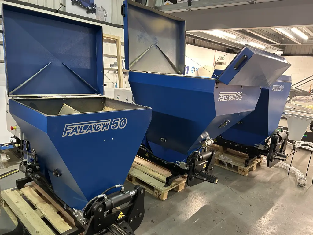 Three blue Falach 50 briquette machines with open lids sitting on wooden pallets inside a workshop