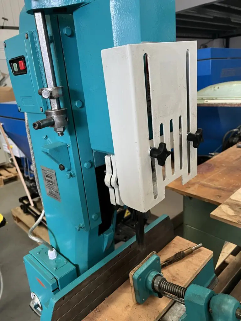 Close-up of a teal Wadkin DM/V vibrating chisel mortiser with a white slotted guard and timber workpiece clamped beneath