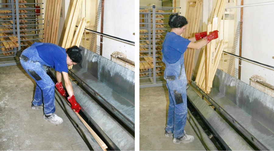 Worker in blue overalls and red gloves using an impregnation and basic coating bath to treat timber lengths in a workshop