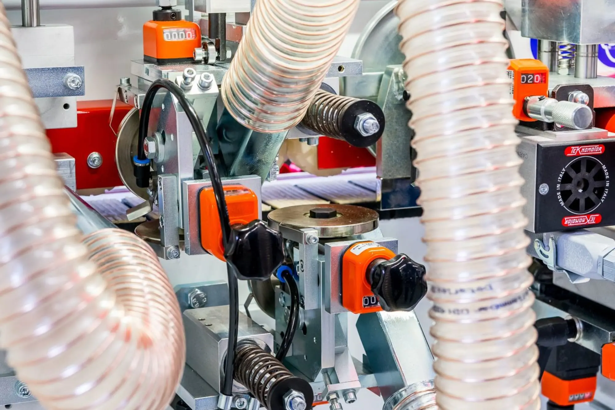 Close-up of the Lange B85KFE edge bander's internal mechanisms, showing orange adjustment knobs, dust extraction hoses, and Teknomotor spindles.
