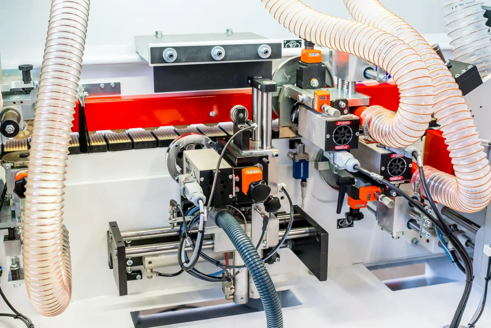 Close-up of a Lange B85KFE edge banding machine showing orange-accented units, dust extraction hoses, and feed rollers.