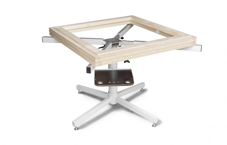 Soukup frame assembling equipment with a square wooden frame held on a white metal cross-base stand with central metal clamp mechanism