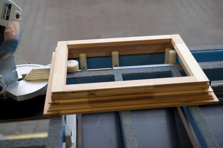 A pine wood frame assembled on a Soukup Assembling Table KS 2400, with clamping pins and a mitre saw visible nearby.
