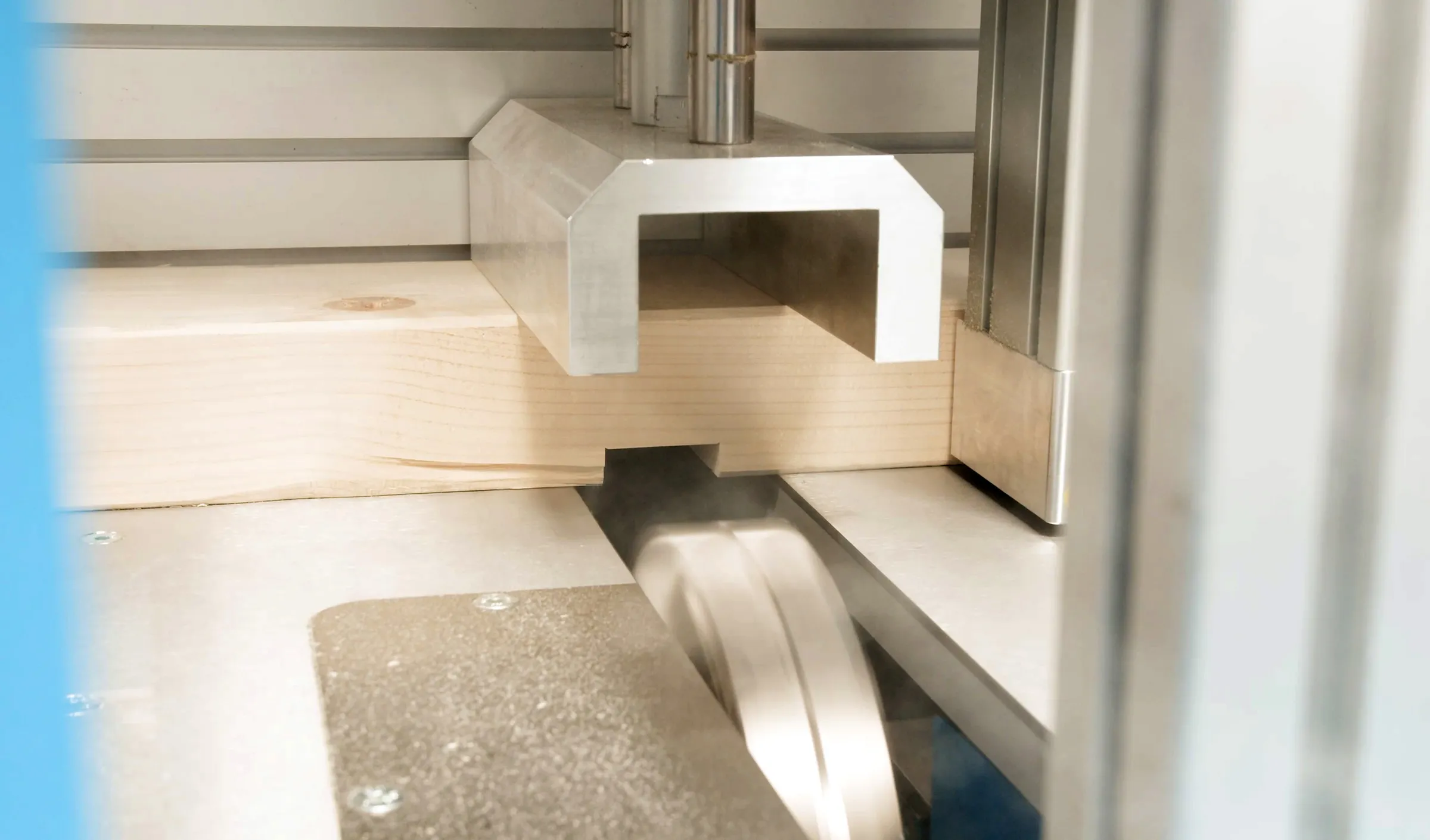 Close-up of a Soukup Crossline 500 cross cut saw blade cutting through a timber plank within a metal-framed machine.