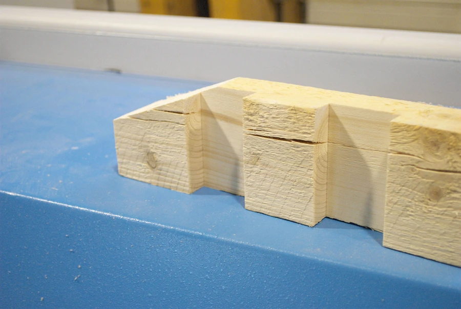 Freshly cut pale timber pieces with interlocking notched joints resting on a blue workshop surface