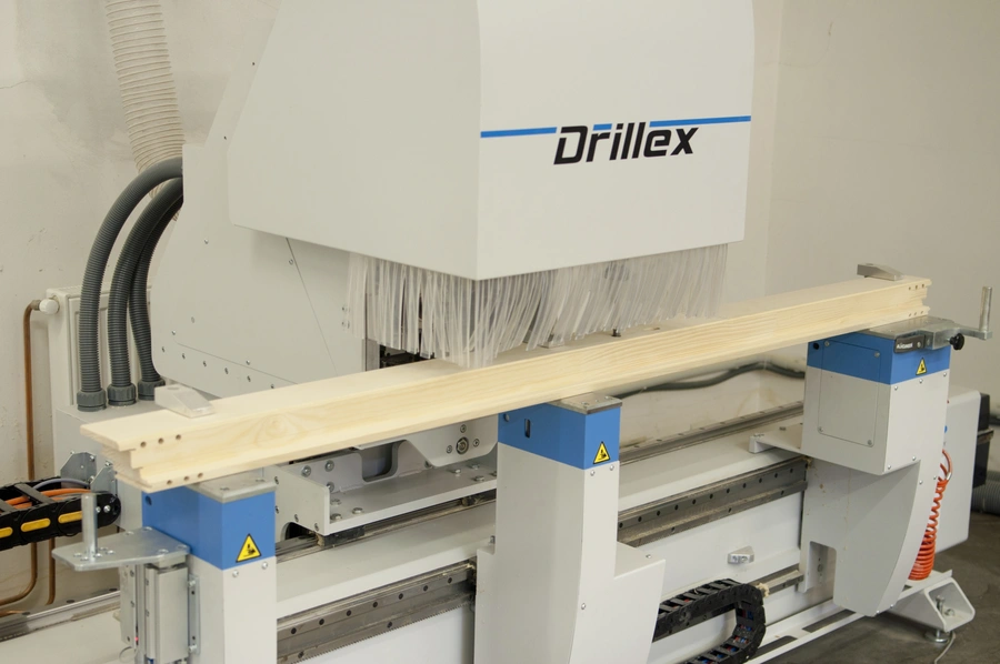 Soukup Drillex work centre machine processing a length of pale timber on its blue and white feed bed