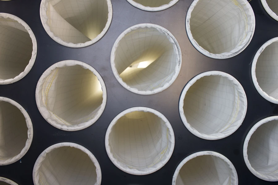 Overhead view of multiple white cylindrical filter bags mounted on a dark metal panel inside a dust extractor unit