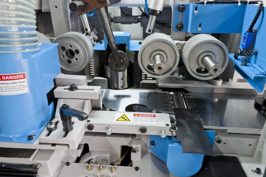 Close-up of blue Soukup fourside planer and moulder machine showing serrated cutter heads and danger warning labels