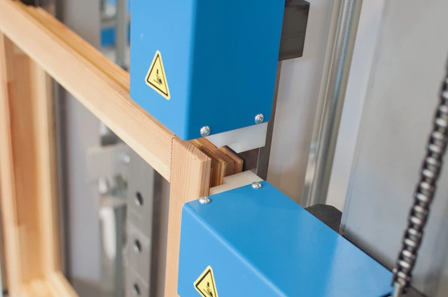 Close-up of a blue industrial window and door press machine clamping a wooden timber frame joint