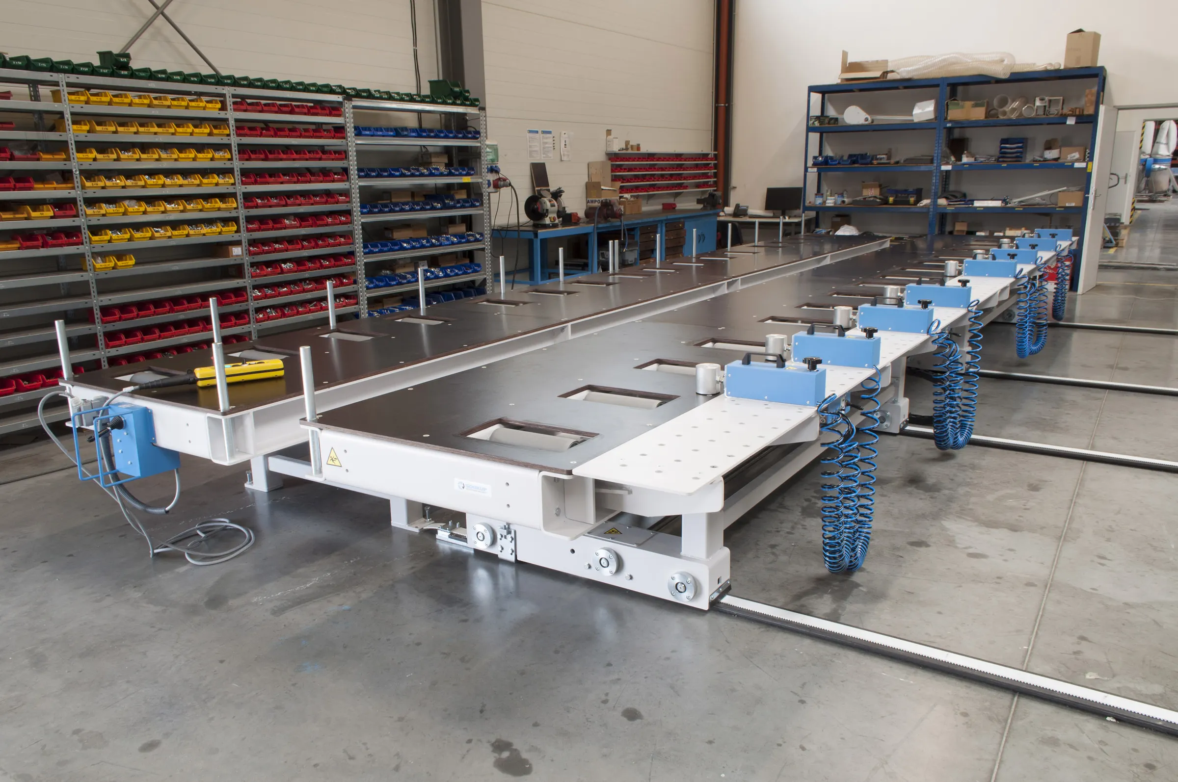 Large white industrial framer line machine with blue components and coiled cables on a factory workshop floor