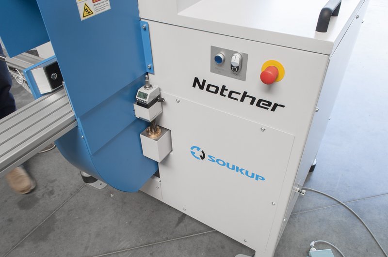 White and blue Soukup Notcher machine with emergency stop button, control panel, and safety warning labels.