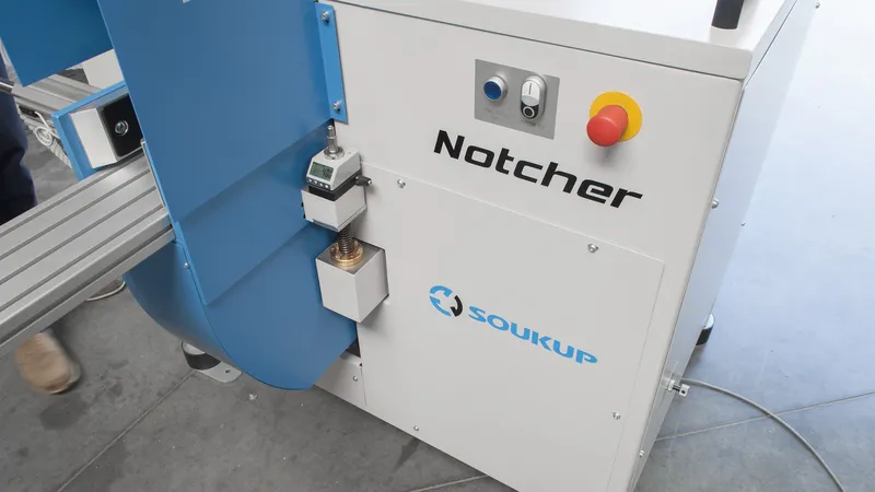 Close-up of a white and blue Soukup Notcher machine with a red emergency stop button and control panel.