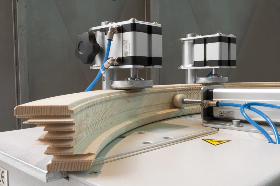 Curved timber segments being pressed and shaped by a Soukup segment press machine with stepper motors and blue pneumatic tubing