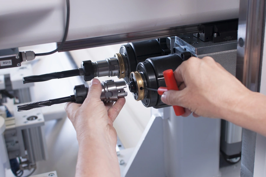 A technician's hands fitting a precision tool holder into a CNC machining centre spindle using a red-handled key.