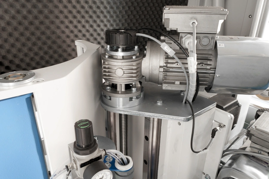 Close-up of an electric motor and spindle assembly mounted on a linear rail within a sound-dampened industrial tenoning machine enclosure