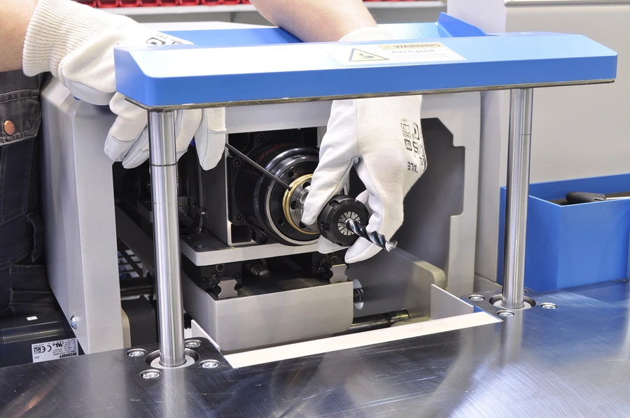 Gloved hands assembling internal mechanical components inside a blue and grey Soukup Versa CNC window machine on a workbench