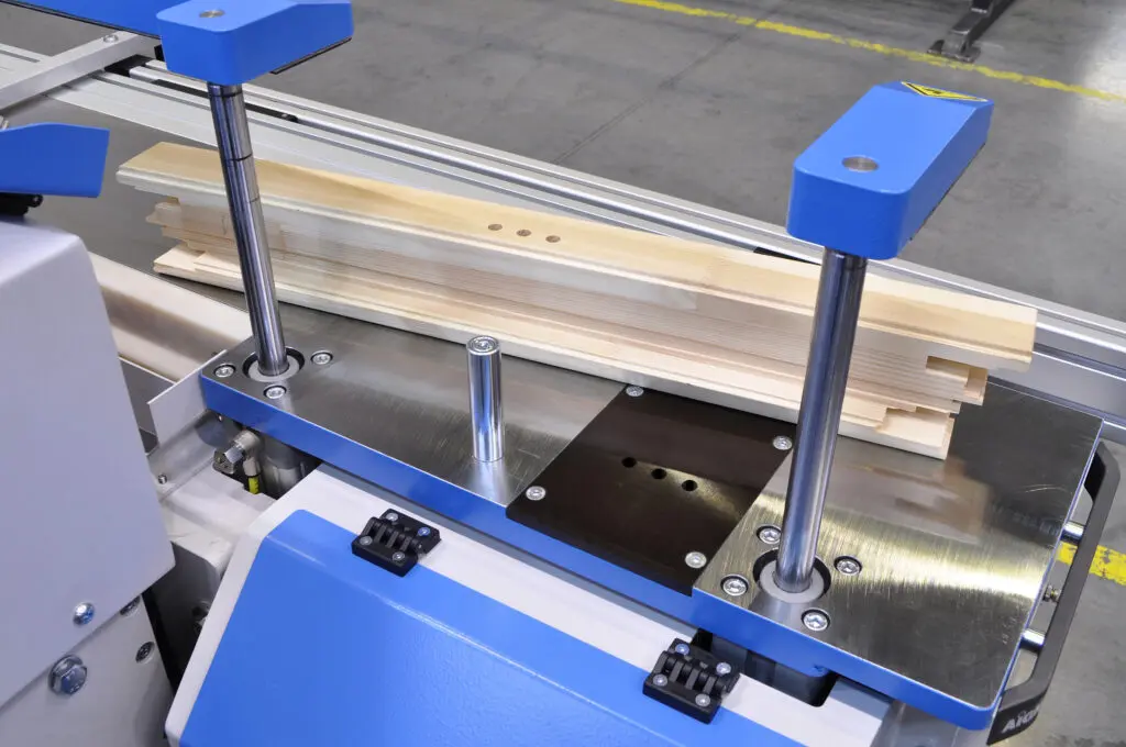 Blue and silver CNC window machine clamping a timber window frame component on a factory production line.
