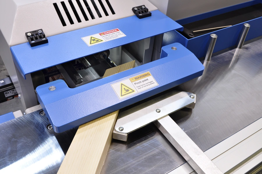 A blue Soukup Versa CNC window machine processing a timber profile, with danger and warning labels visible on the unit.