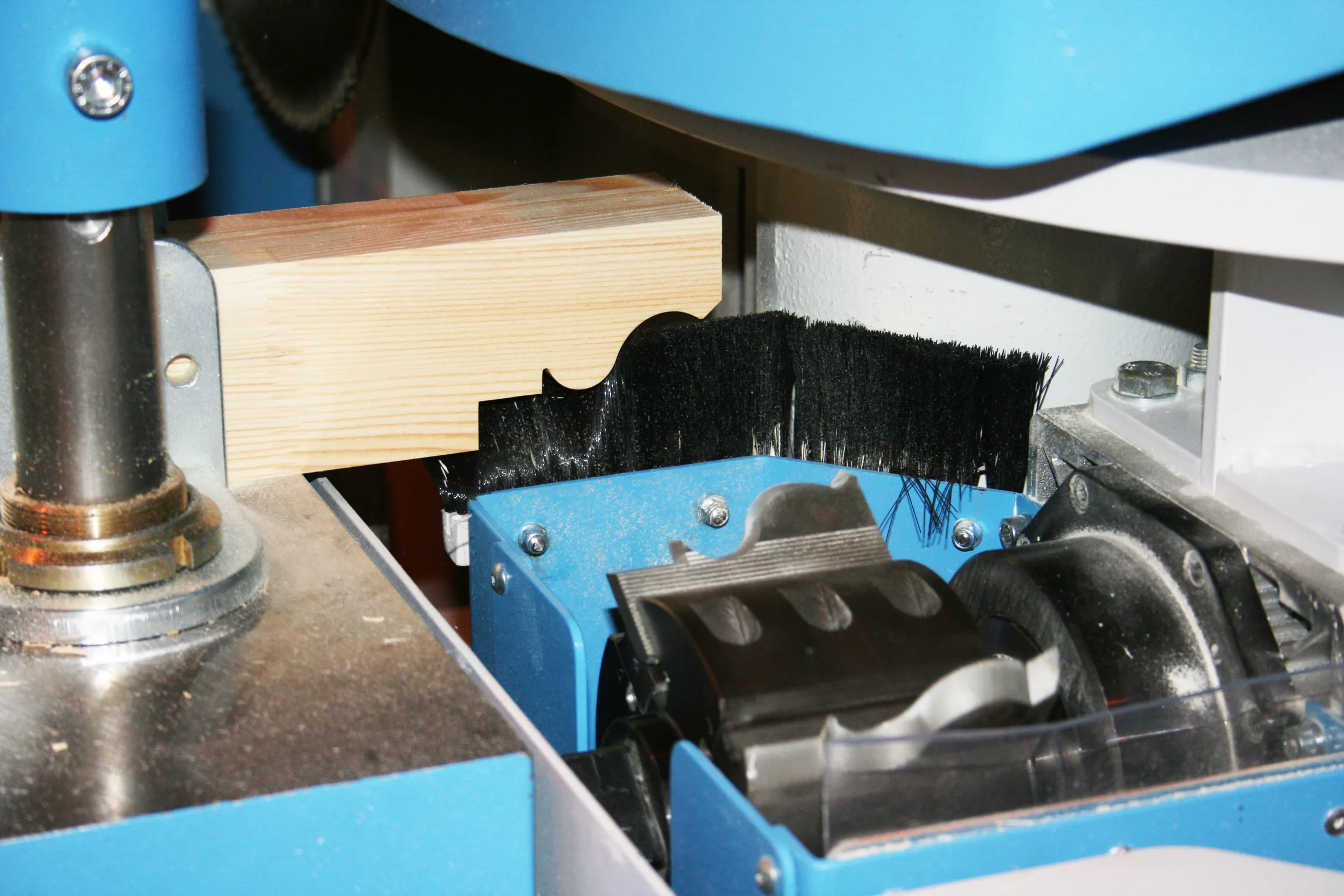 Close-up of a timber profile being shaped by a rotating cutter head and brush seals on a blue CNC window machine