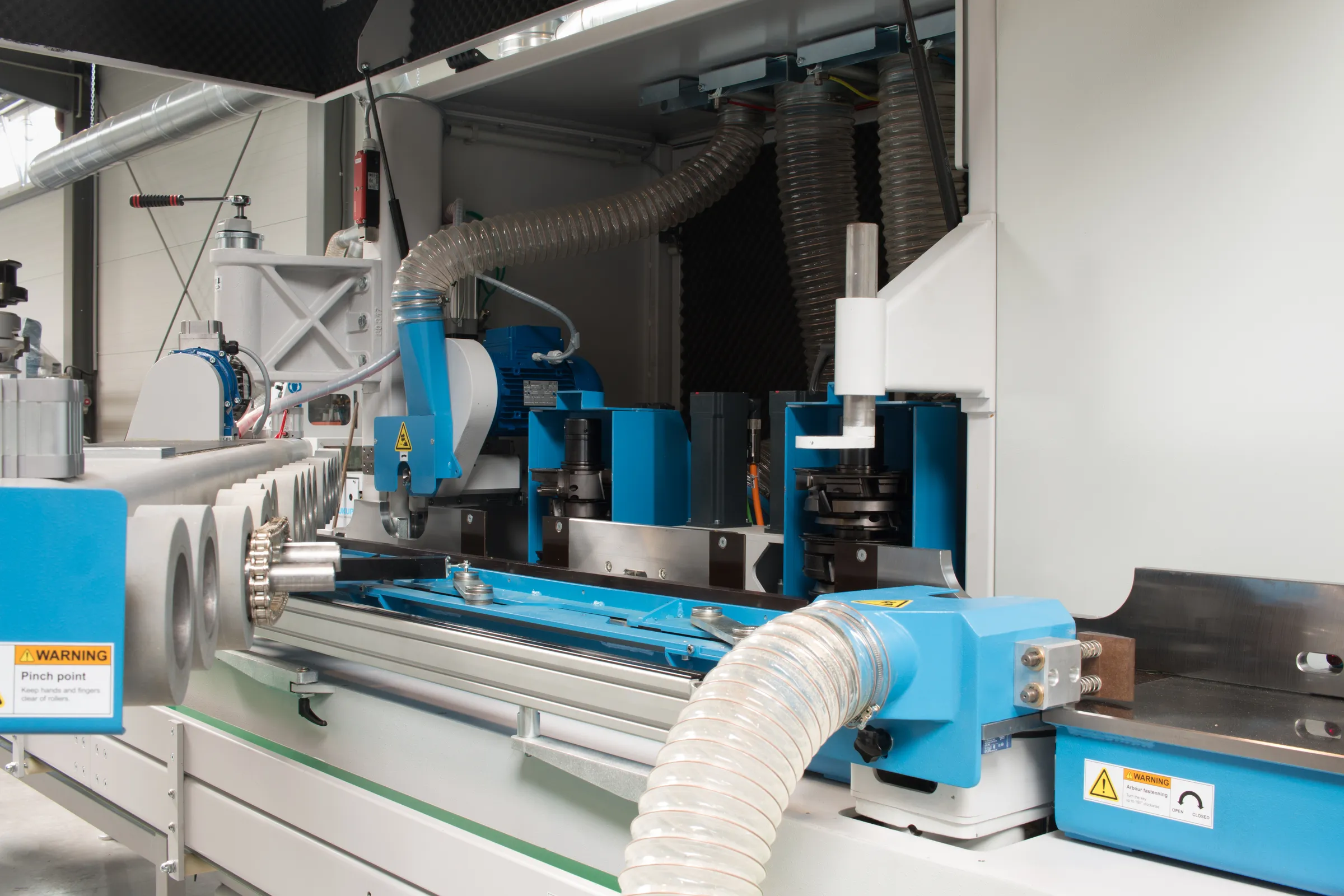 Interior view of a Soukup Wizard 3S CNC window machine showing blue motorised spindles, dust extraction hoses and warning labels