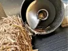 Close-up of a metal shredder intake funnel surrounded by loose dry straw and wood chip debris on a dark metal surface
