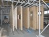 Timber frame wall panels with door and window openings stored upright on blue track brackets inside a factory workshop.