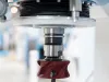 Close-up of a CNC machine spindle with a red milling cutter head and drill bit attached, set in a blue industrial frame