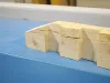 Freshly cut pale timber pieces with interlocking notched joints resting on a blue workshop surface