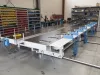 Large white industrial framer line machine with blue components and coiled cables on a factory workshop floor