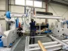 Two engineers assembling a large CNC machine in an industrial workshop, with cables, hoses and components being installed.