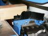 Close-up of a timber section being fed through a blue CNC window machining centre with brush seals and profiled rollers