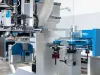 Close-up of a blue and silver CNC machining centre with rotating tool changer, drill bits, and a router bit in a factory