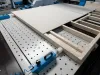 Large flat panels resting on a wooden slatted frame atop a perforated industrial machine table in a factory