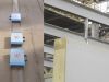 Three blue metal track clamps fixed to a concrete rail, alongside a timber frame panel with a steel fixing bolt in an industrial building