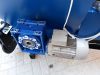 Blue worm gearbox and grey electric motor mounted on a blue Falach 70 briquette machine, resting on paved ground