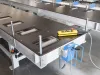 Industrial framing machine worktable with roller conveyors, a yellow pendant control box with emergency stop, and blue electrical housing unit