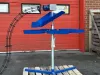 Blue IWM Six Bag Carousel Unit with top loading, mounted on a steel pole and cross-base frame, displayed on a wooden pallet outdoors.