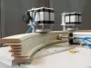 Curved timber segments being pressed and shaped by a Soukup segment press machine with stepper motors and blue pneumatic tubing