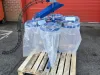 Blue IWM six bag carousel unit with top loading, wrapped in clear plastic on a wooden pallet outside a red industrial building