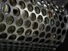 Close-up of a perforated metal shredder screen with circular holes revealing worn cutting blades beneath