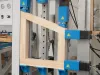 Wooden window frame held in a blue industrial press machine during manufacturing assembly