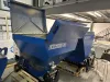 Blue Falach 50 briquette machine with open lid on a pallet inside an industrial workshop, with a Falach 100 visible behind it