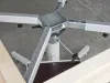 Underside of a white metal table base assembly with a central steel column, cross-frame arms, and adjustable feet on a concrete floor