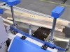 Blue and silver CNC window machine clamping a timber window frame component on a factory production line.