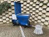 Blue Falach 50 briquette machine with open lid and control panel, displayed on brick paving beside a white collection bag